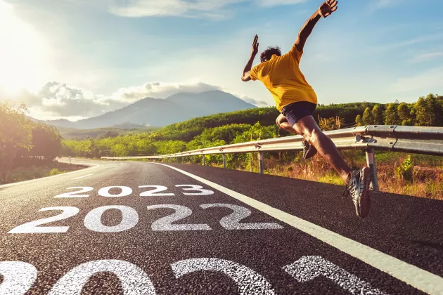 En man som springer snabbt på väg med årtalet 2022 och 2023 målat på asfalten. Foto.