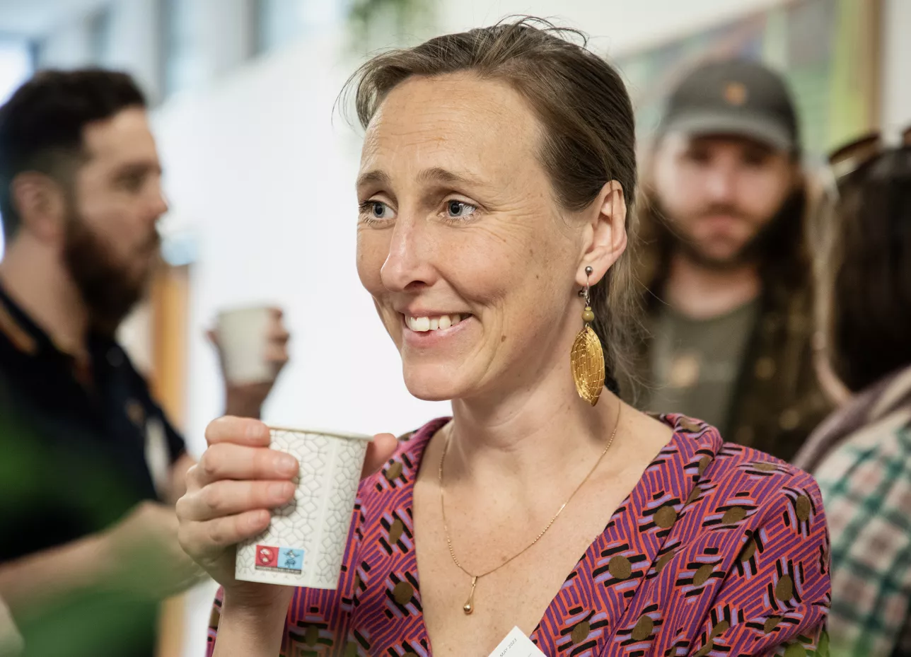 A woman with a coffee mug with people in the background. Photo.