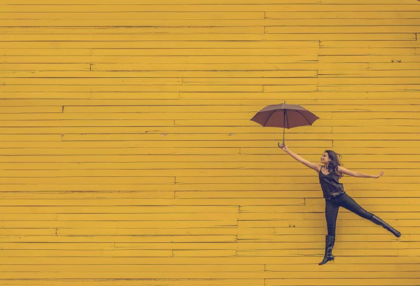 Female jumping, holding an umbrella, yellow background. Photo.
