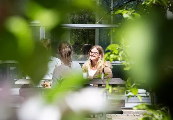 People sitting at a table outside CEC's building. They are surrounded by greenery. Photo.