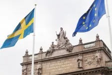 En del av riksdagshuset samt Sveriges och EUs flaggor. Foto.