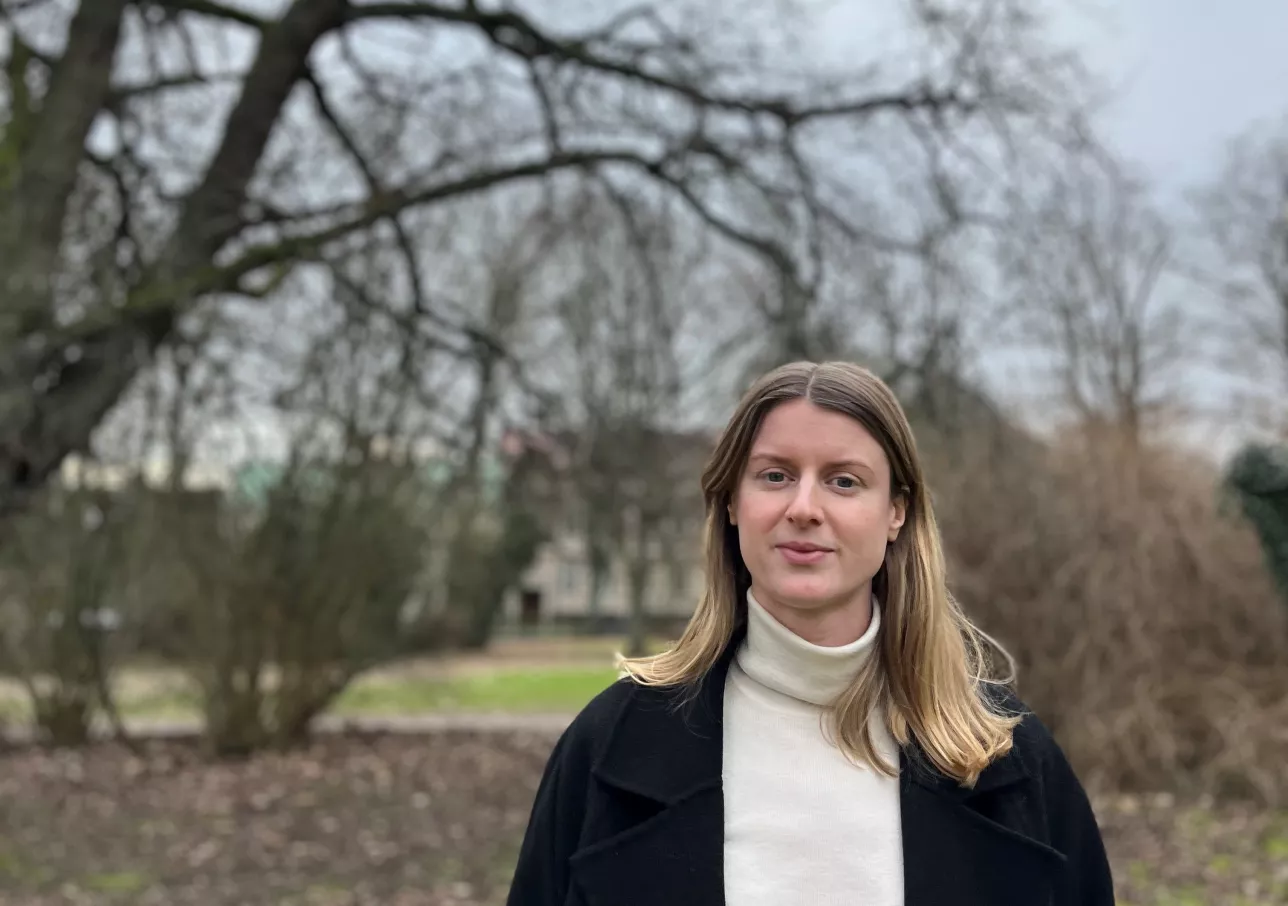 Sara Ullström står utomhus framför ett träd. Foto.
