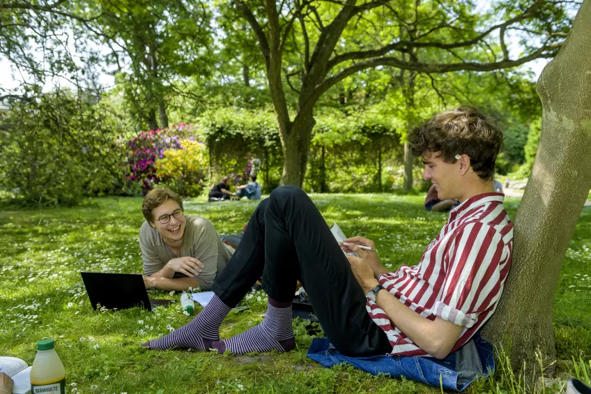 Två unga män som sitter på en gräsmatta och studerar. Foto.