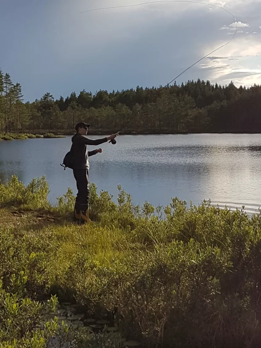 En man står och fiskar vid en sjö. Foto.